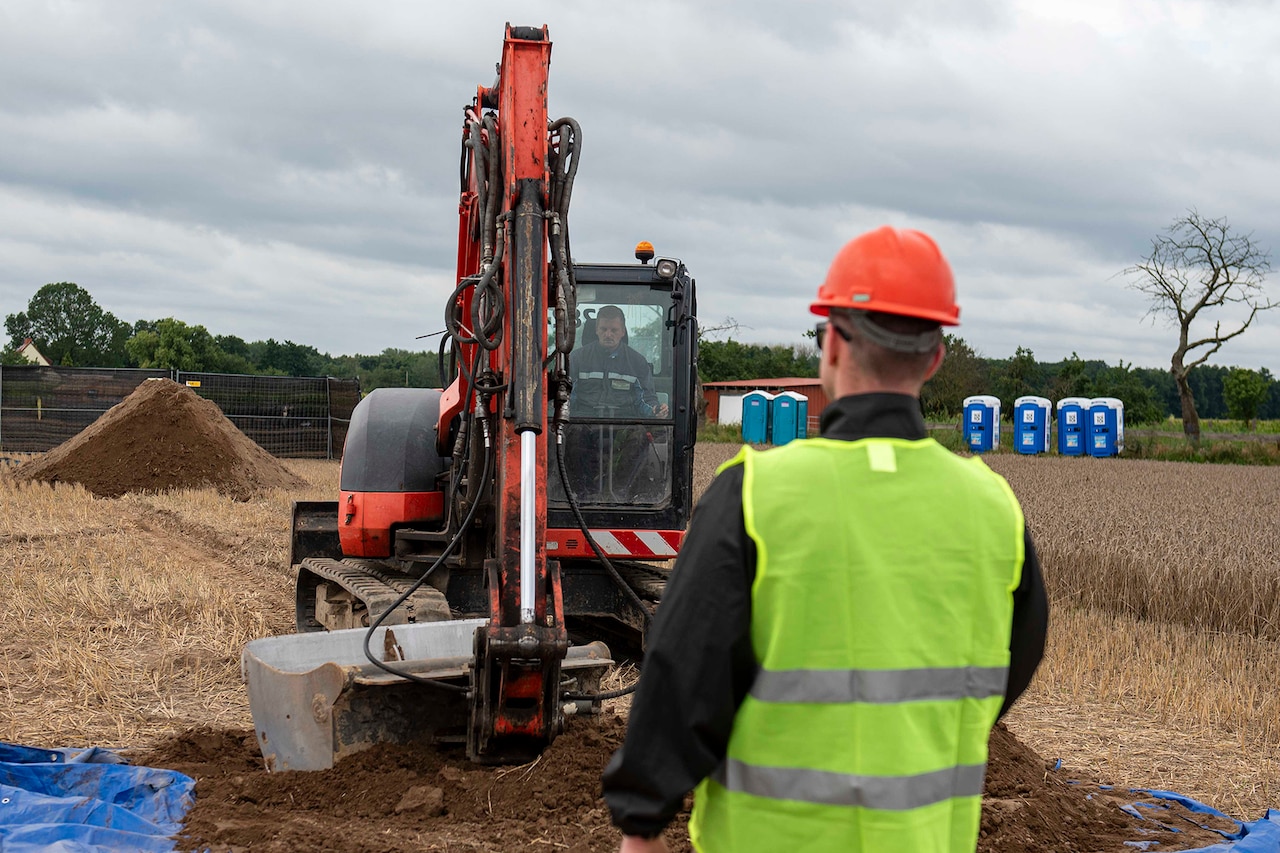 A heavy equipment operator gets directions from worker as they work in a field.