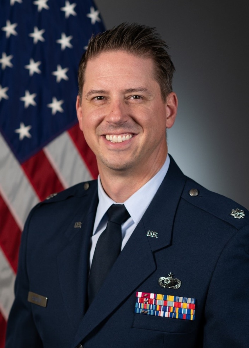 man in uniform poses in front of flag