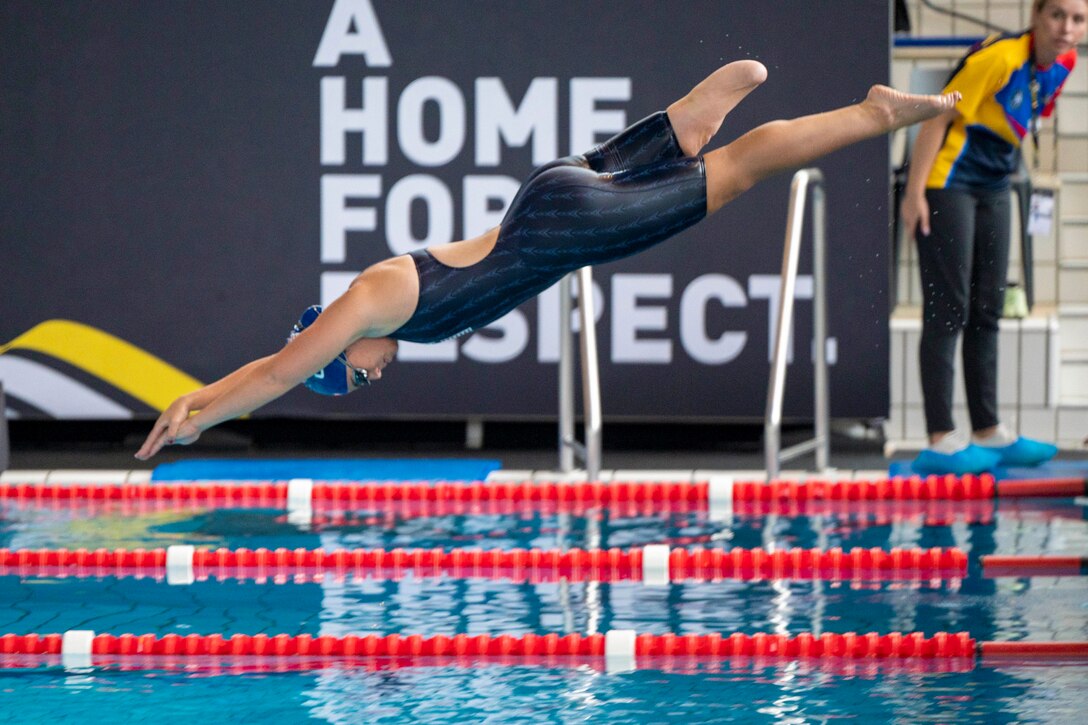 A retired Marine dives into a pool during a competition as a person watches.