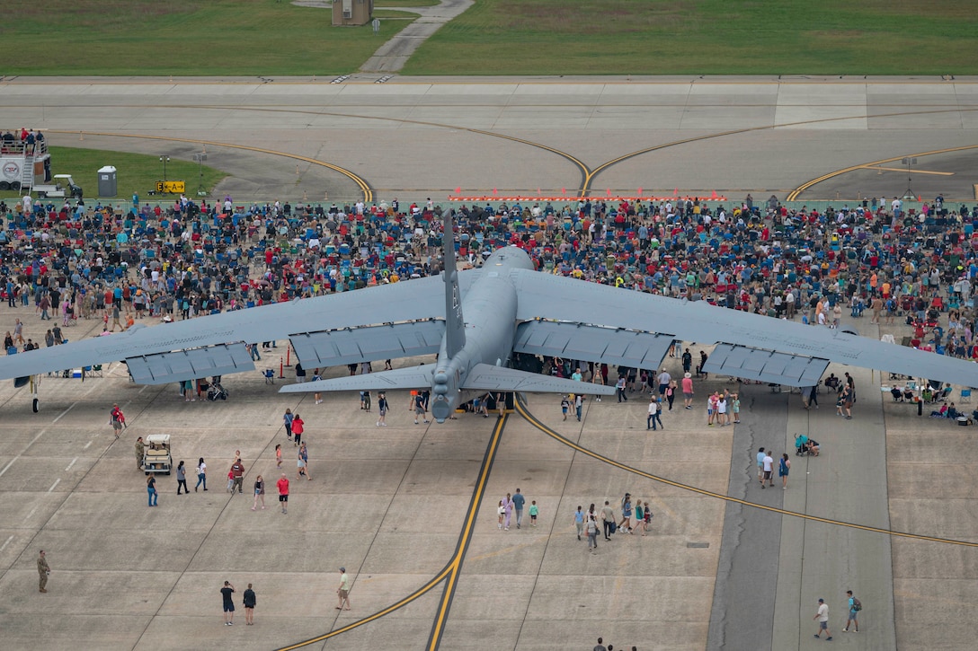 Dozens of spectators gather around an aircraft parked on a tarmac as seen from above.