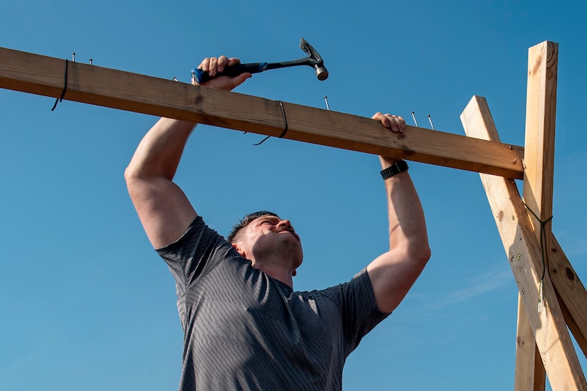 An airman hammers nails in a wood beam overhead.