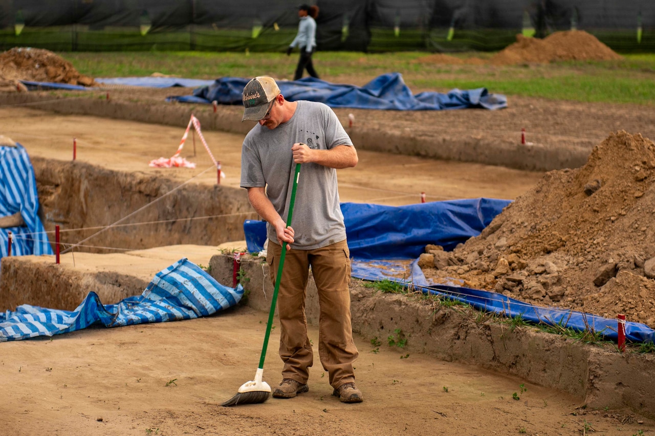 A Marine sweeps an outdoor dirt plot.