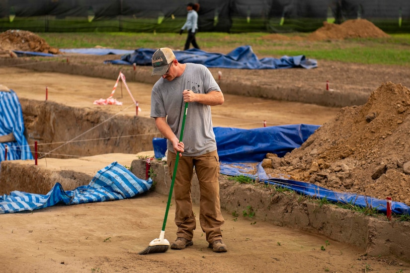 A Marine sweeps an outdoor dirt plot.