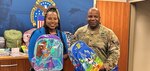 civilian woman and man in uniform hold children's backpacks