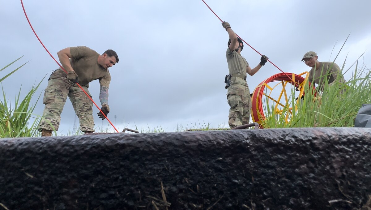 (Left to right) U.S. Air Force Staff Sgt. William Johnson, 374th Contracting Squadron NCO in charge of resource advisors and YokoWERX project lead, Airman 1st Class Gabrielle Oropesa, and Senior Airman Carlos Reyes, 374th Communications Squadron cable antenna technicians, feed a pull string into a duct rodder at Yokota Air Base, Japan, Aug.23, 2023. YokoWERX recruited personnel from multiple units to assist with fixing the south runway control lights to include the 374th Civil Engineer Squadron and the 374th Operations Support Squadron. (Courtesy Photo)