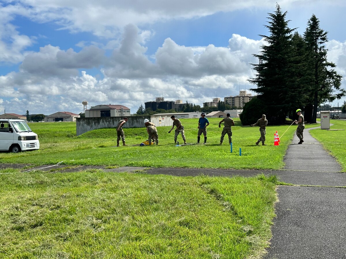 Members of the 374th Communications Squadron and 374th Contracting Squadron pull a cable toward the south runway overrun control lights at Yokota Air Base, Japan, Aug. 24, 2023. The new system installation required feeding about 3,000 feet of cable through multiple manholes to connect it to the lights and the air traffic control tower. (Courtesy Photo)