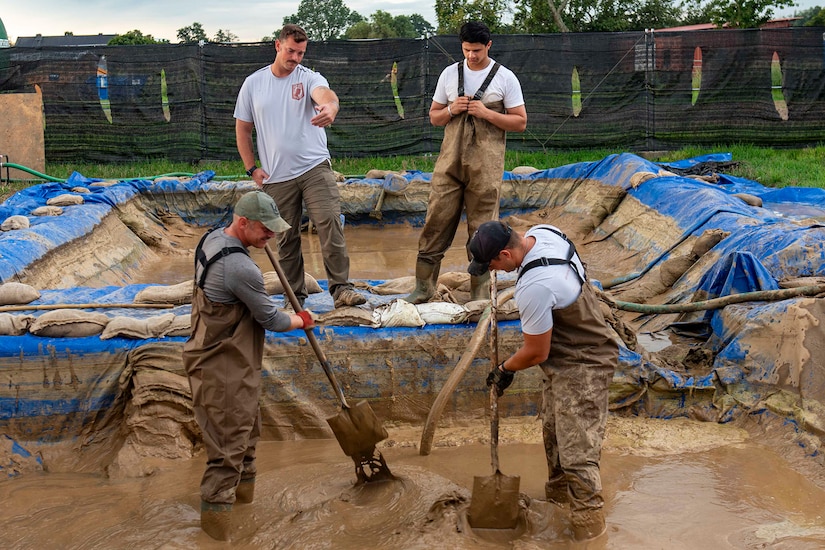 People use shovels to sort through mud in one of two large pits.