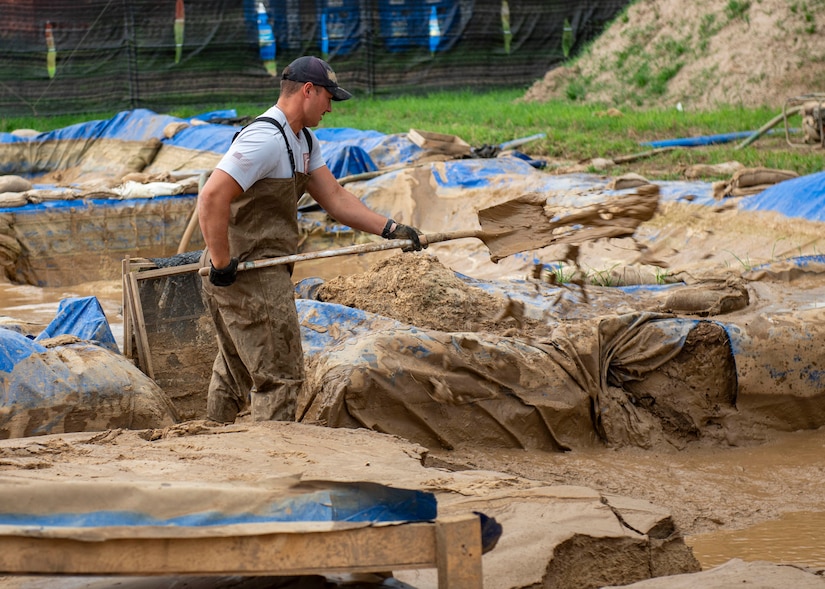 A man shovels mud in a large pit draped with tarps.