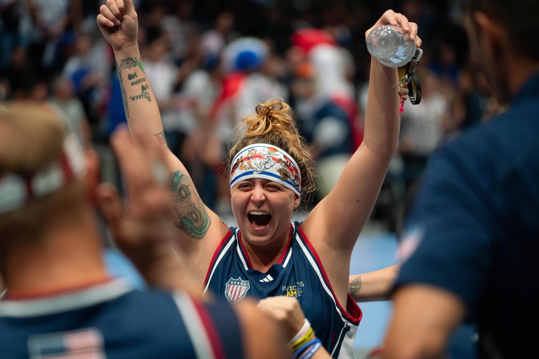 An athlete in a wheelchair raises their hands and smiles.