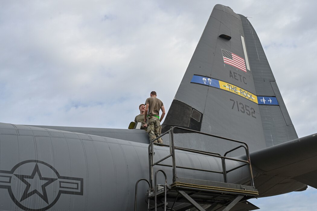 Airmen stand on top of an aircraft.