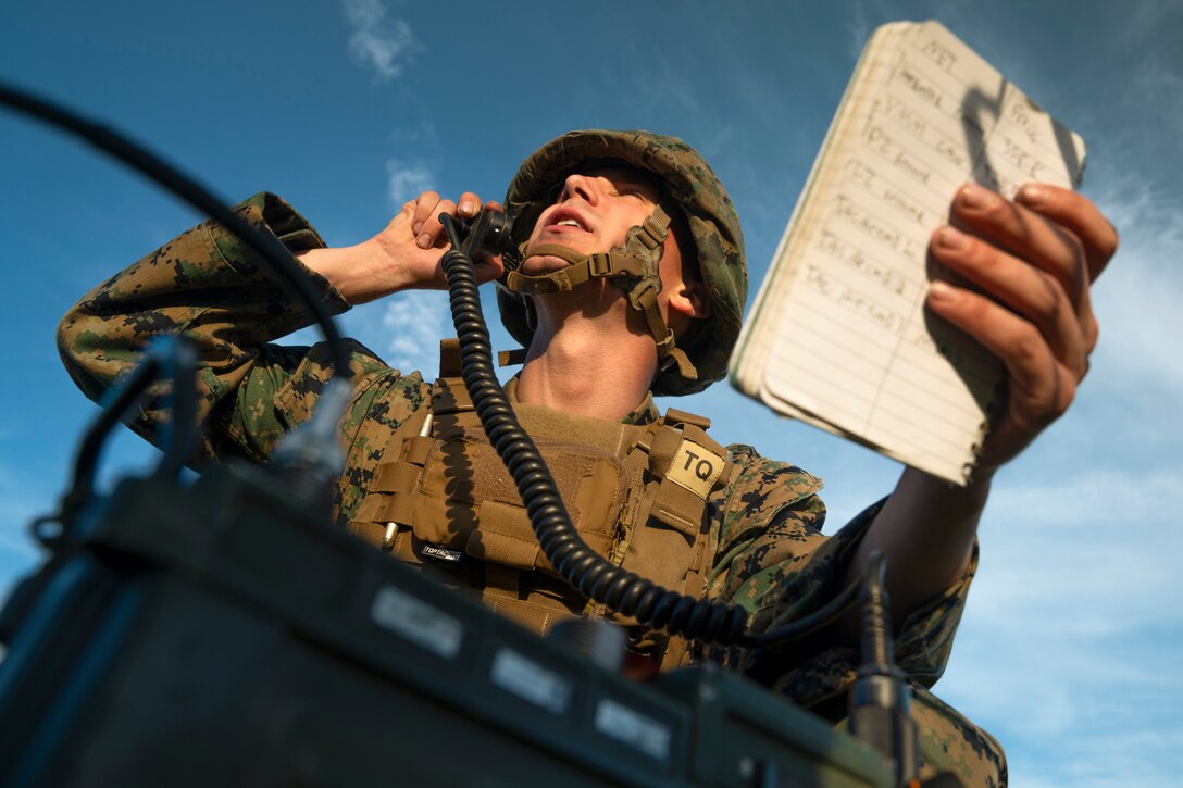 A Marines speaks on the phone while holding a journal as seen from below.