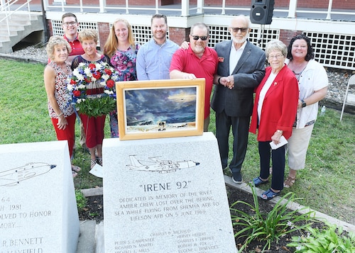 Men and women pose behind a gray concrete memorial