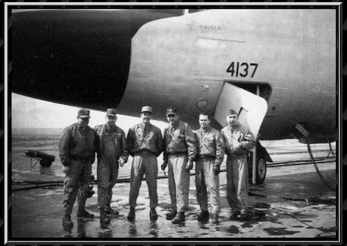 Black and white photo of six men standing under an aircraft's nose