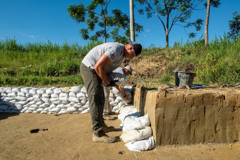 A person works places sandbags around an excavated area.