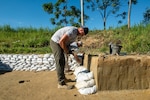 A person works places sandbags around an excavated area.
