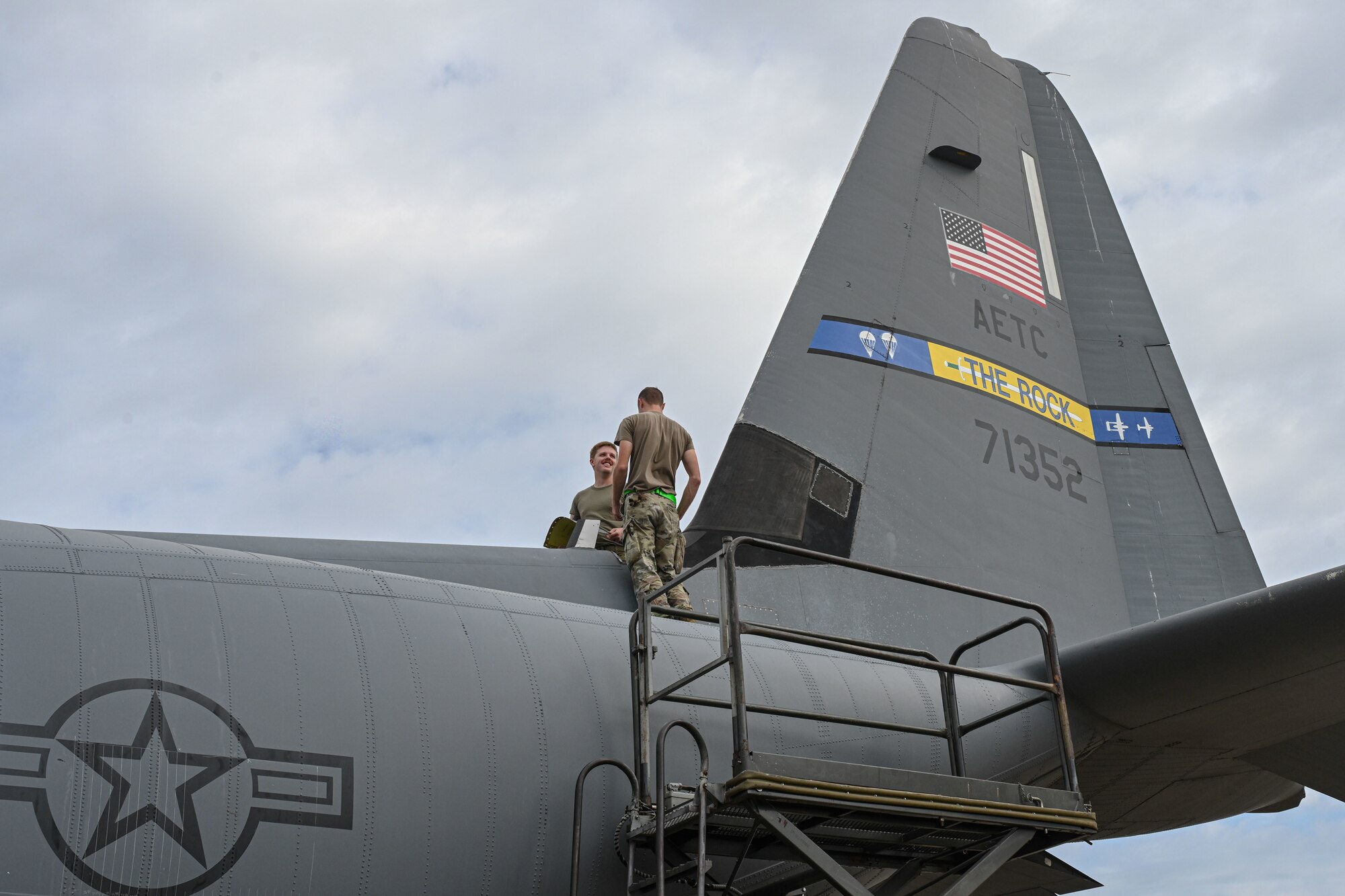 Airmen stand on top of an aircraft.