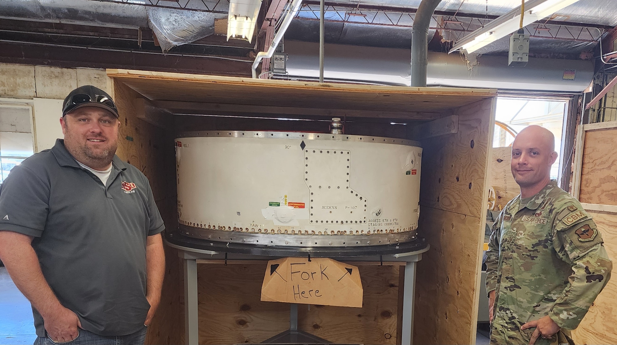 Two men stand beside a box with a PSRE trainer in it