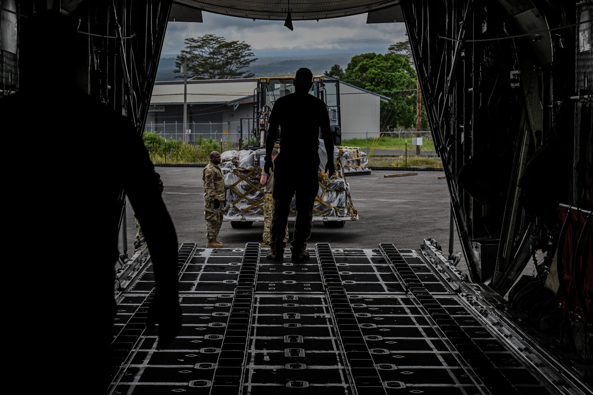 U.S. Air Force loadmaster directs a forklift operator carrying cargo to be loaded onto a C-130H Hercules aircraft.