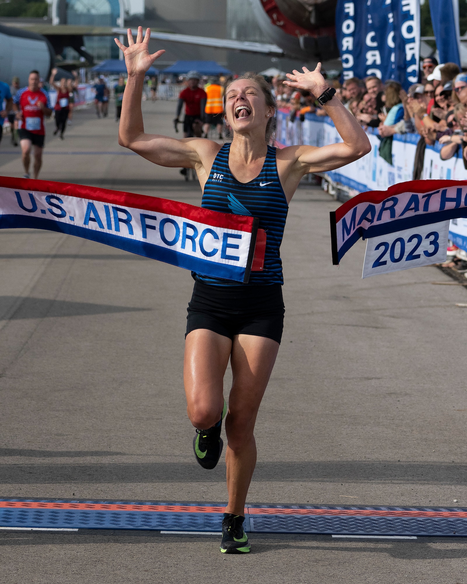 A woman in raises her arms as she breaks through a red, white and blue banner with "U.S. Air Force Marathon" on it.