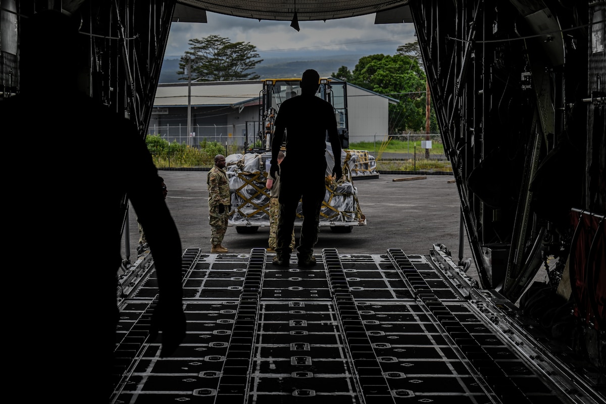 U.S. Air Force loadmaster directs a forklift operator carrying cargo to be loaded onto a C-130H Hercules aircraft.