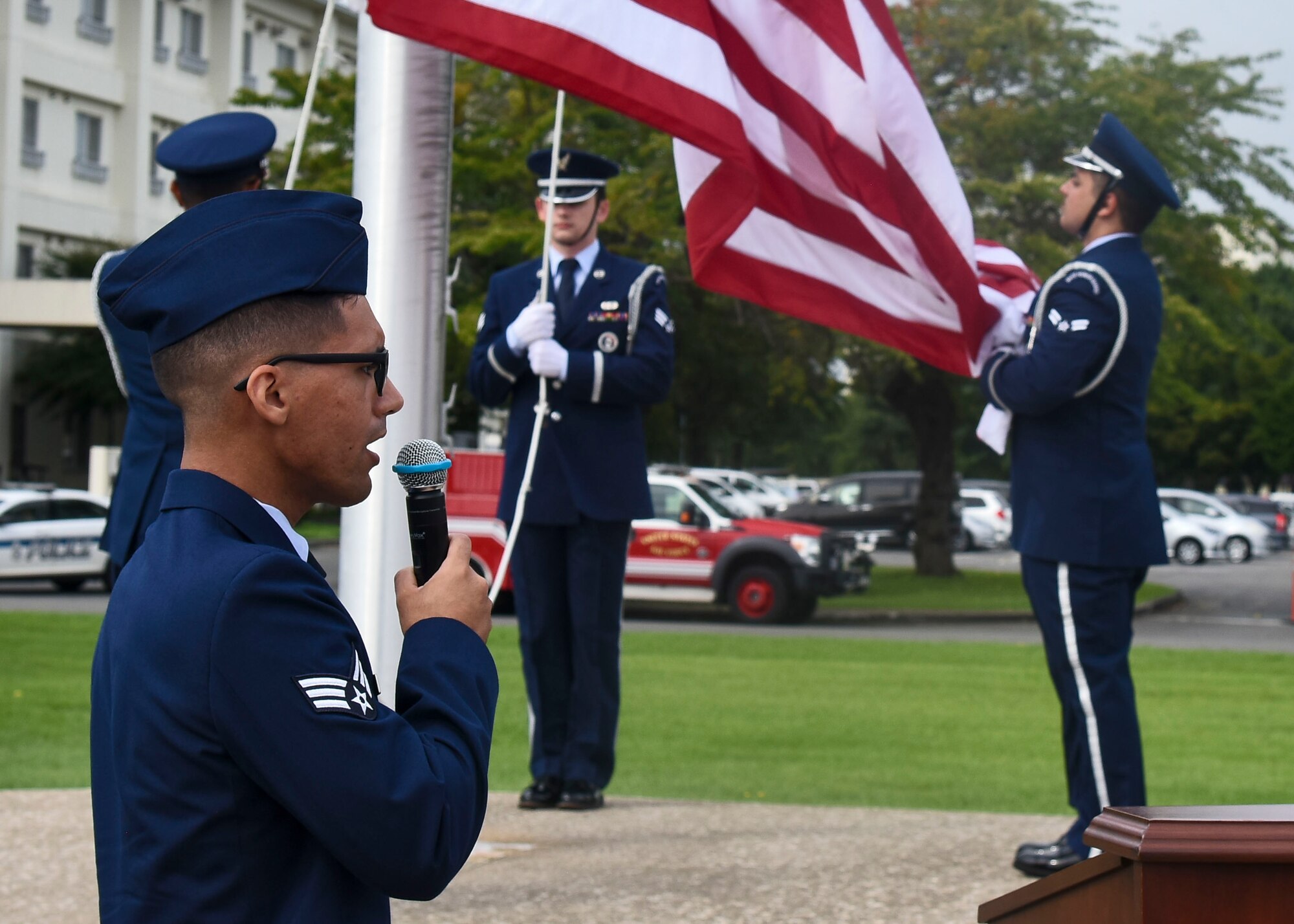 A service member sing the U.S. national anthem while honor guardsmen retrieve the U.S. flag.
