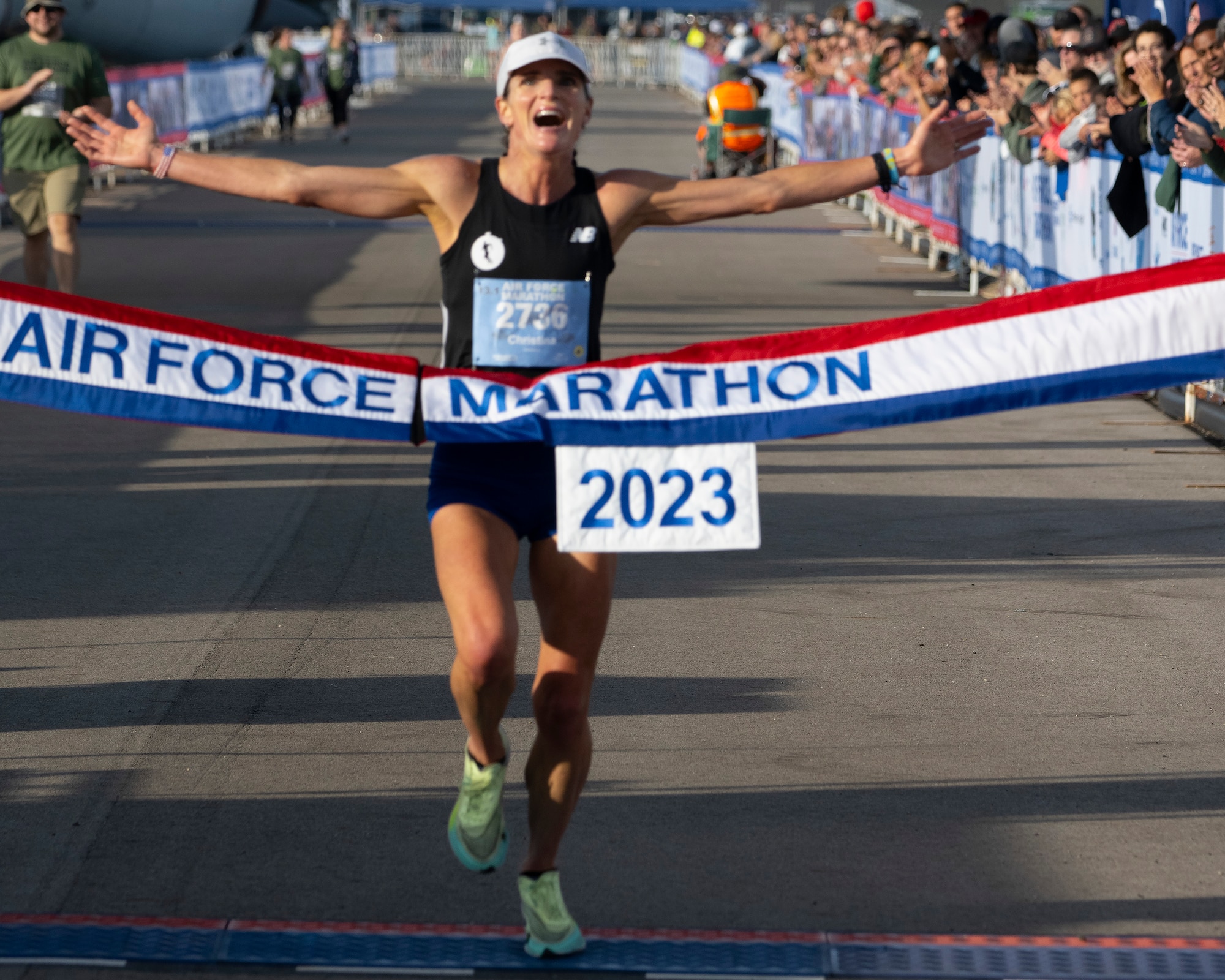 A woman stretches out her arms as she approaches a banner that has "Air Force Marathon" on it.