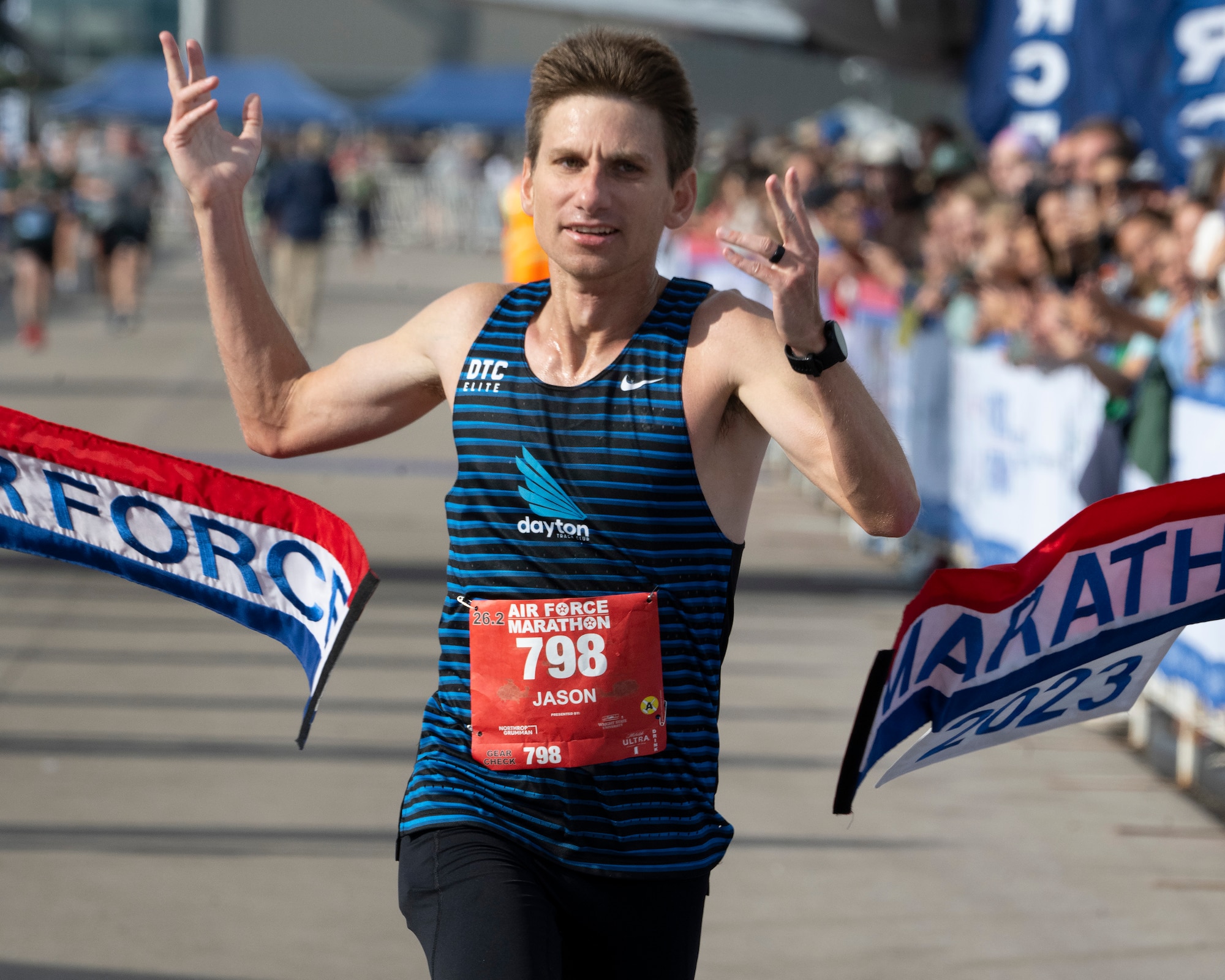 A man raises his arms as he breaks a red, white and blue banner.