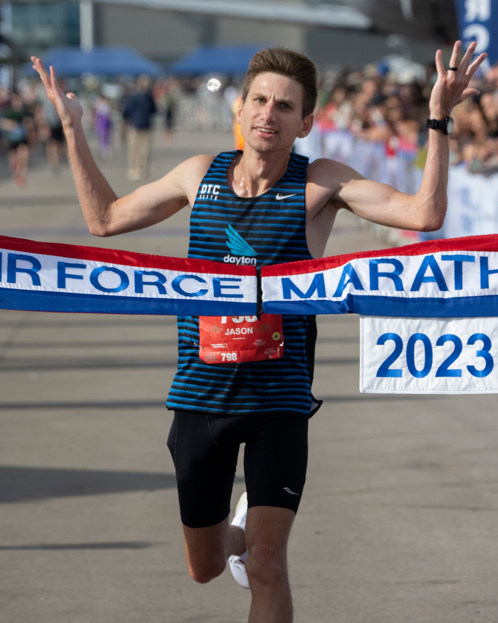 Man raises his arms as he approaches a red, white and blue banner that has "Air Force Marathon" on it.