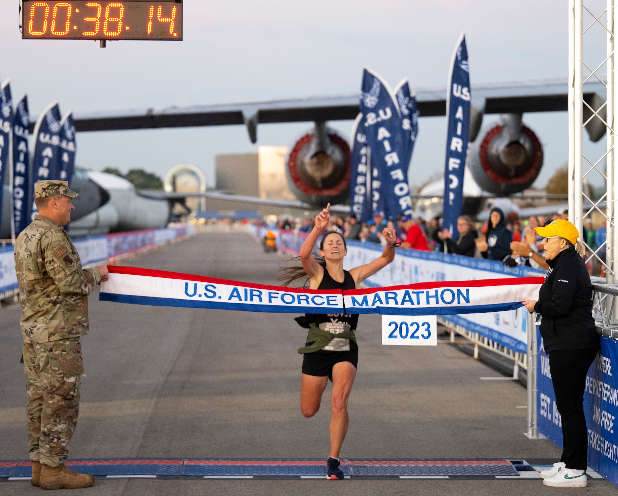 A woman in black athletic clothes raises her arms as she approaches a red, white and blue banner with "U.S. Air Force Marathon" on it.