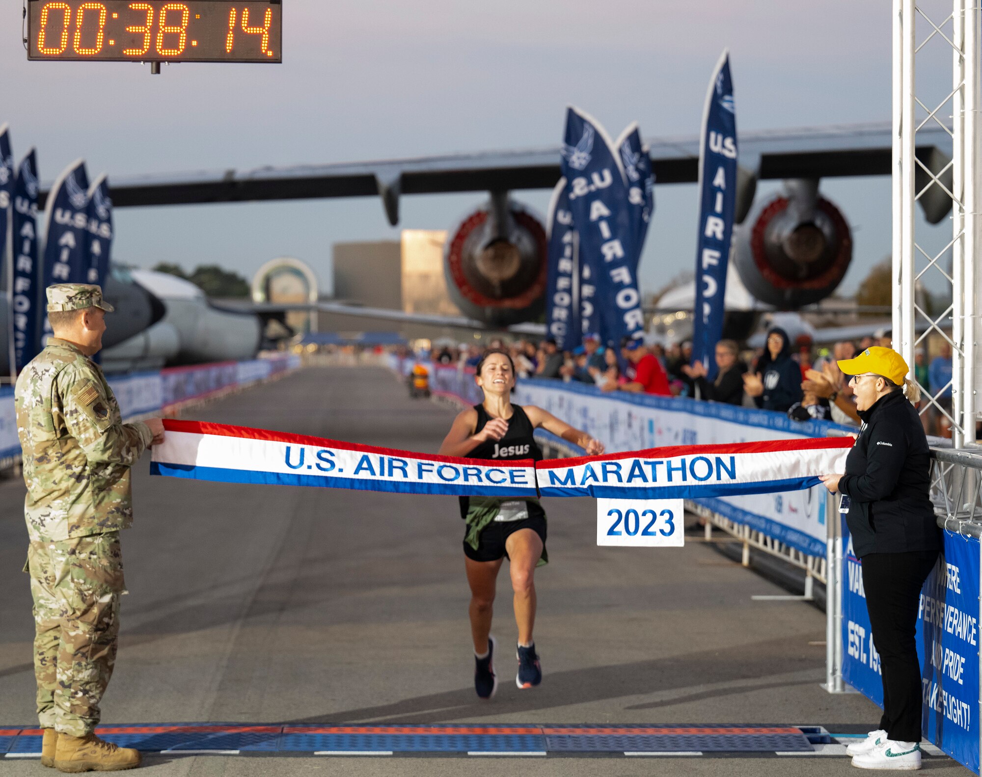 A woman in black athletic clothes raises her arms as she approaches a red, white and blue banner with "U.S. Air Force Marathon" on it.