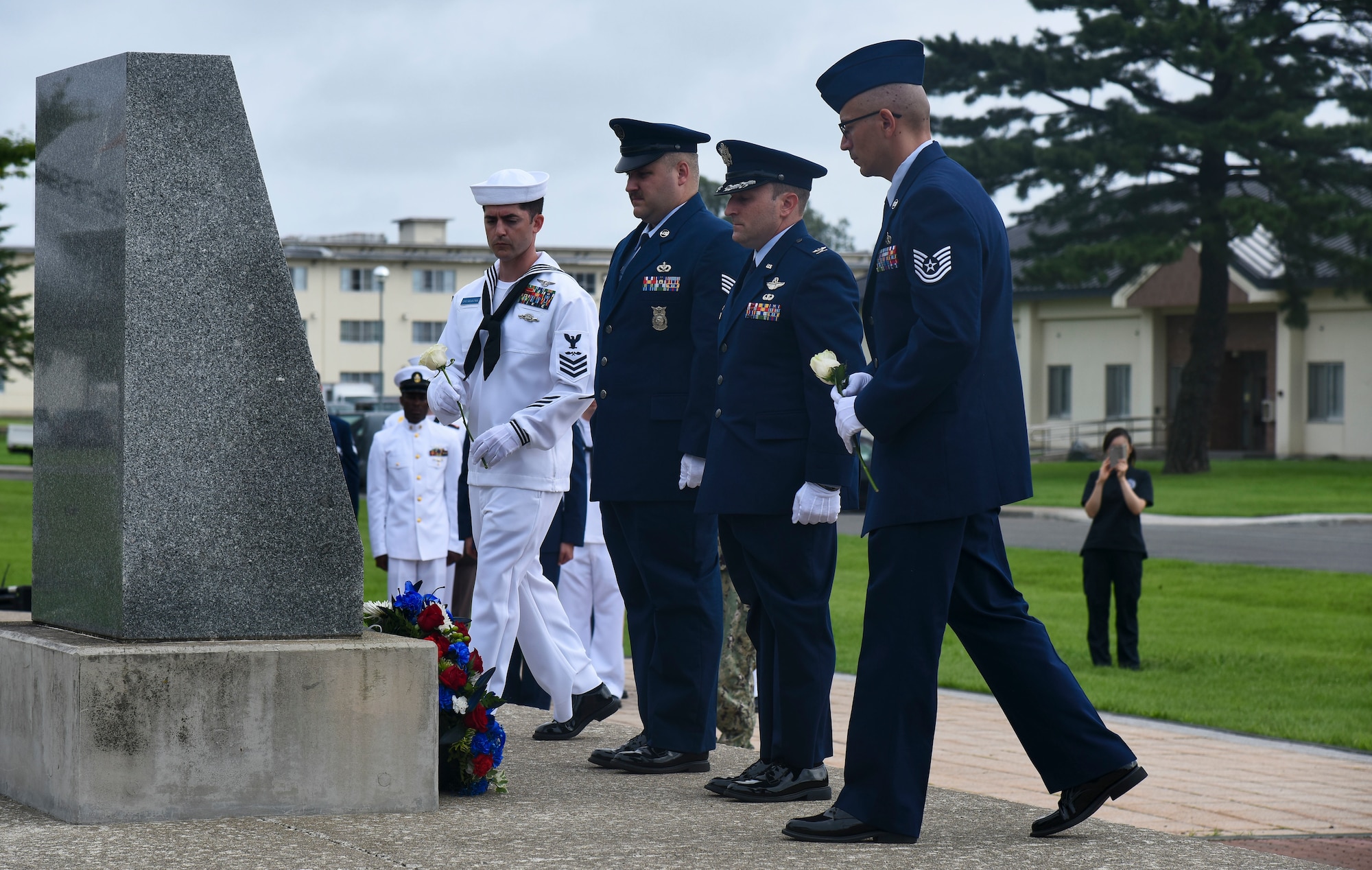 Military members lay flowers in front of a memorial
