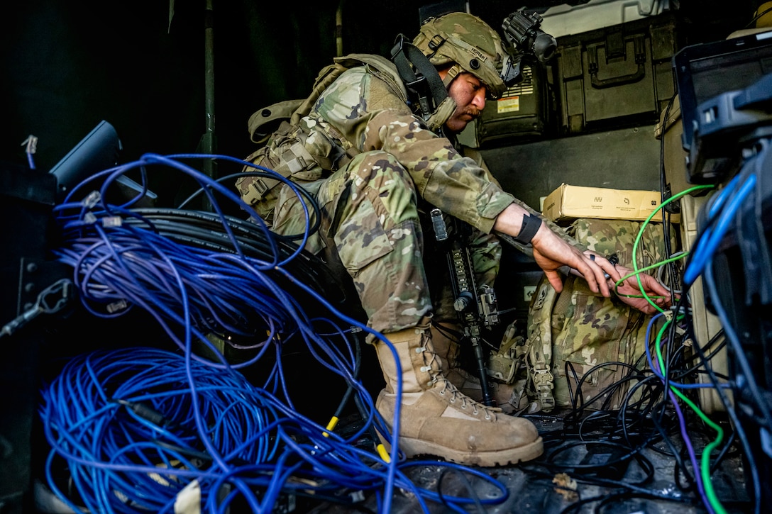 A soldier surrounded by cables reconnects them to a communication system after a drone attack.
