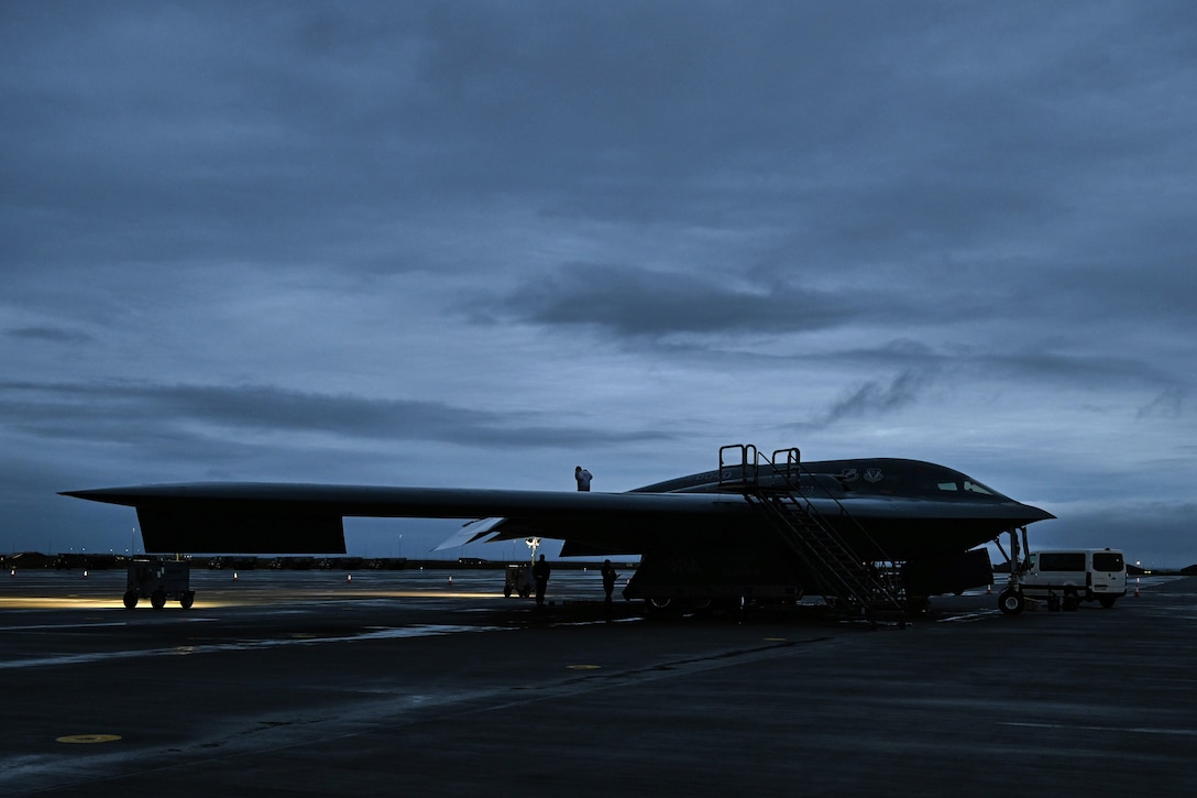 A B-2 Spirit sits on a flight deck at night while soldiers perform maintenance work.