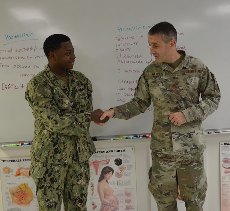 Hospital Corpsman Second Class Douglass Jones is presented with a coin from the Medical Education and Training Campus Commandant, Col. David Walmsley, for Jones' outstanding attention to detail while conducting a practice scan on a student, leading him to recognize an abnormality that allowed the student to receive expedited care for a mass that could have later become symptomatic.