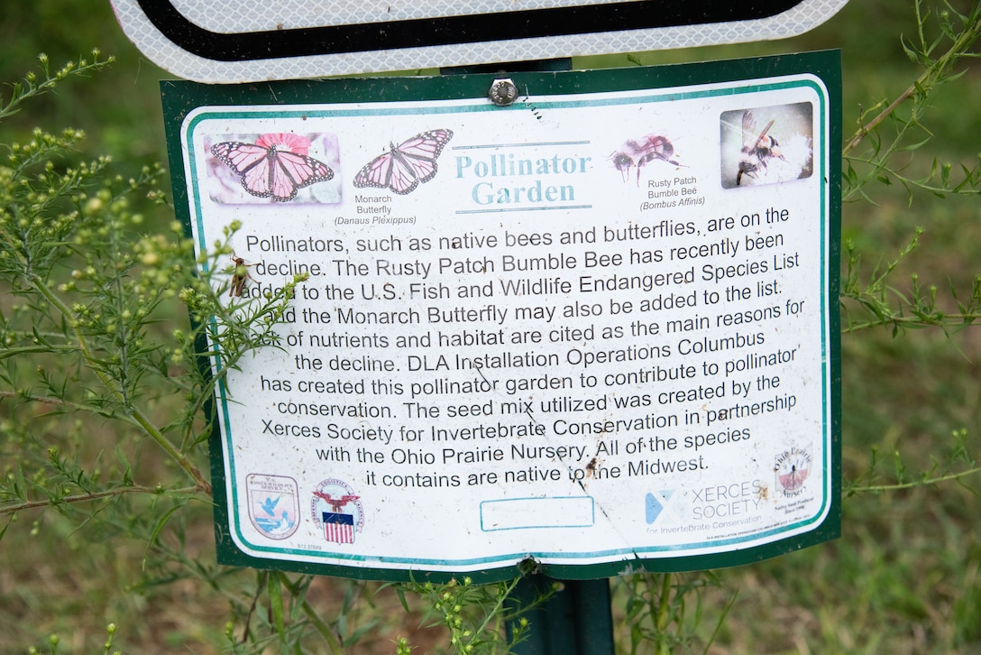 A informational sign sits in front of a large prairie habitat with warm season grasses and flowers.