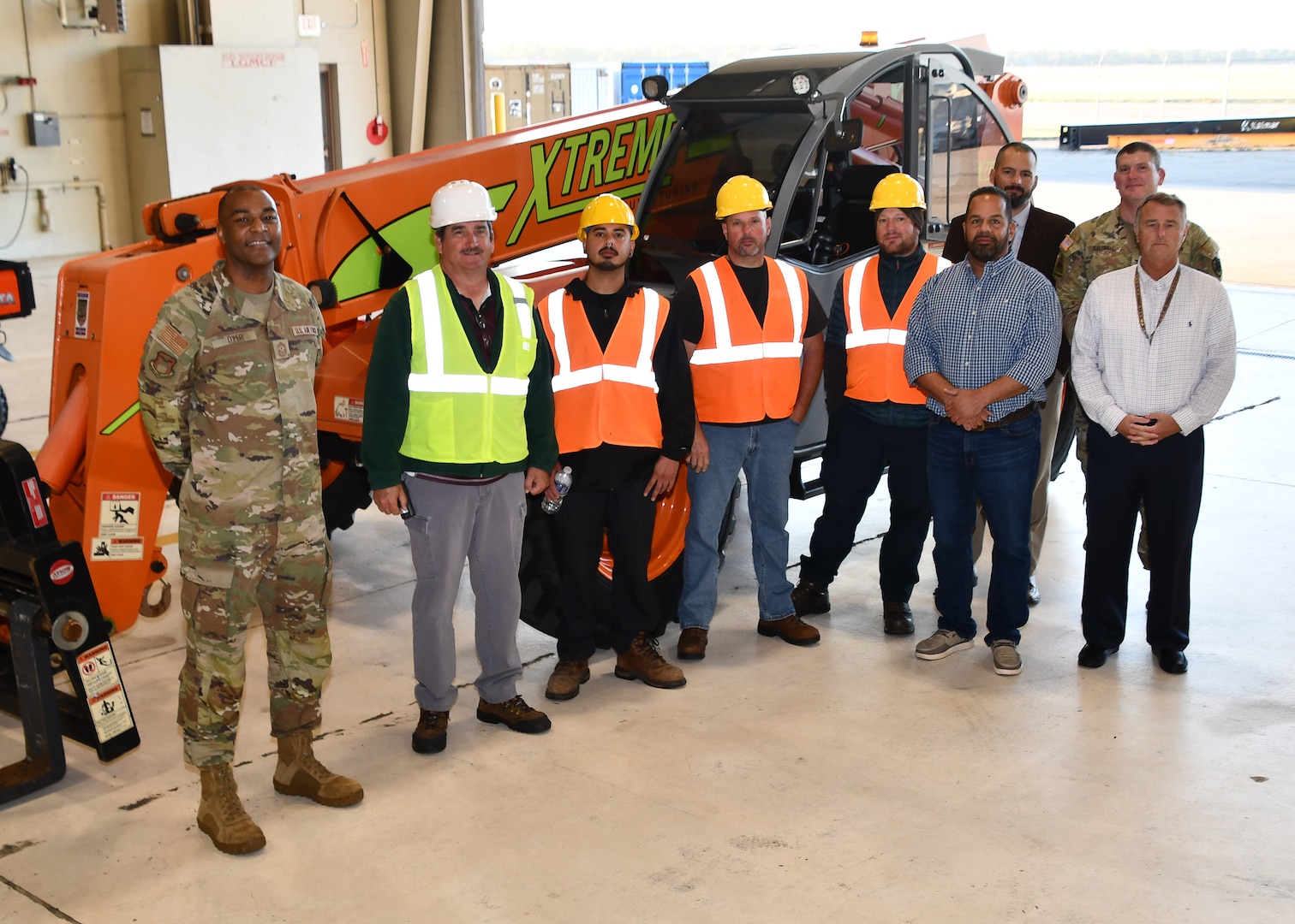 group shot in front of machinery to include soldier, civilians in construction gear and other business professionals