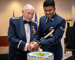 Two Airmen cut a cake together with a sword.