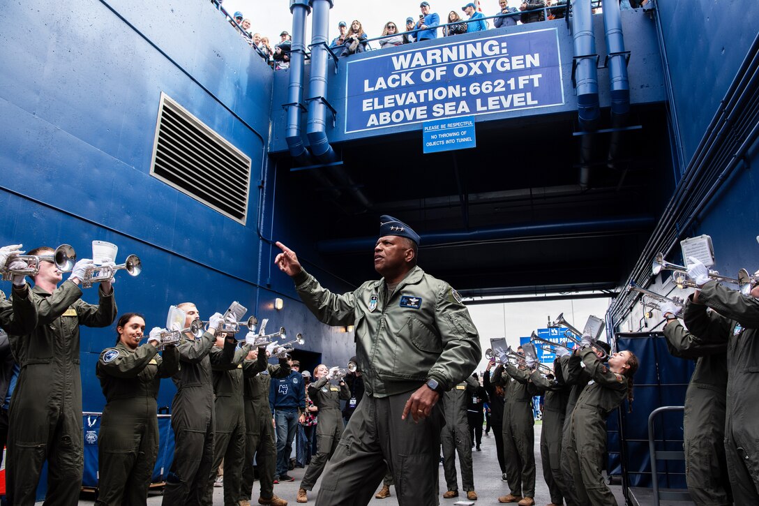 A military officer joins a band and fans in the tunnel of a football stadium.