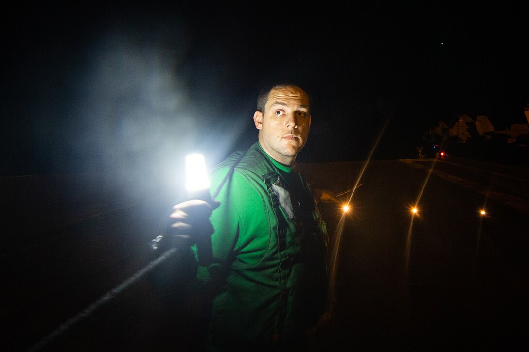 A sailor holds a safety line and flashlight at night.