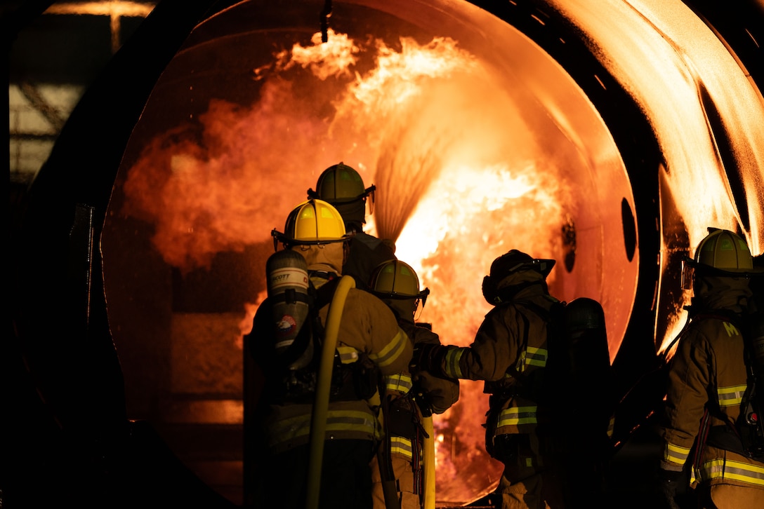 Marines in firefighting gear hose down a fire during training.