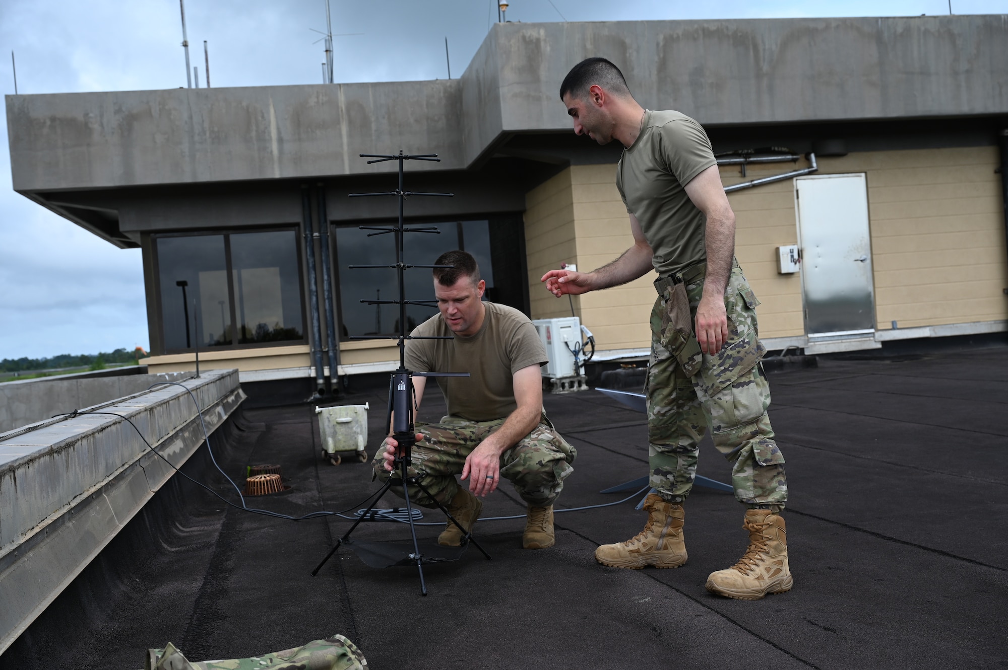 two men in military uniforms set up a communications antenna outside