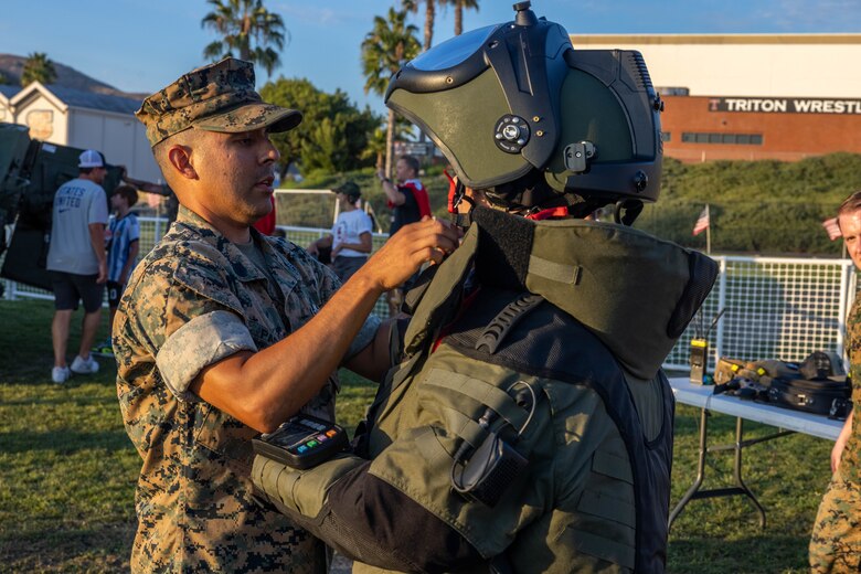 U.S. Marine Corps Gunnery Sgt. Paul I. Padilla, an explosive ordnance disposal technician with Marine Wing Support Squadron 372, Marine Aircraft Group 39, 3rd Marine Aircraft Wing, helps a student put on a bomb suit during San Clemente High School’s military appreciation day at Thalassa Stadium, San Clement, California, Sept. 8, 2023. Padilla demonstrated the equipment used by EOD Marines to locate, neutralize, and dispose of hazards with remote control robots and a bomb suit to students and parents of San Clemente High School. (U.S. Marine Corps photo by Lance Cpl. Jennifer Sanchez)