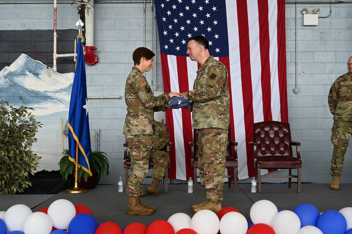 A woman in uniform hands a man in uniform a folded flag.