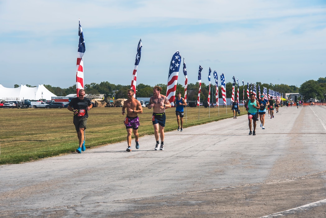 A group of runner run past American flag banners on a road.