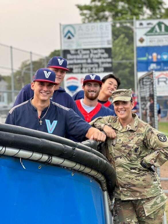 Female soldier poses with four members of a baseball team.