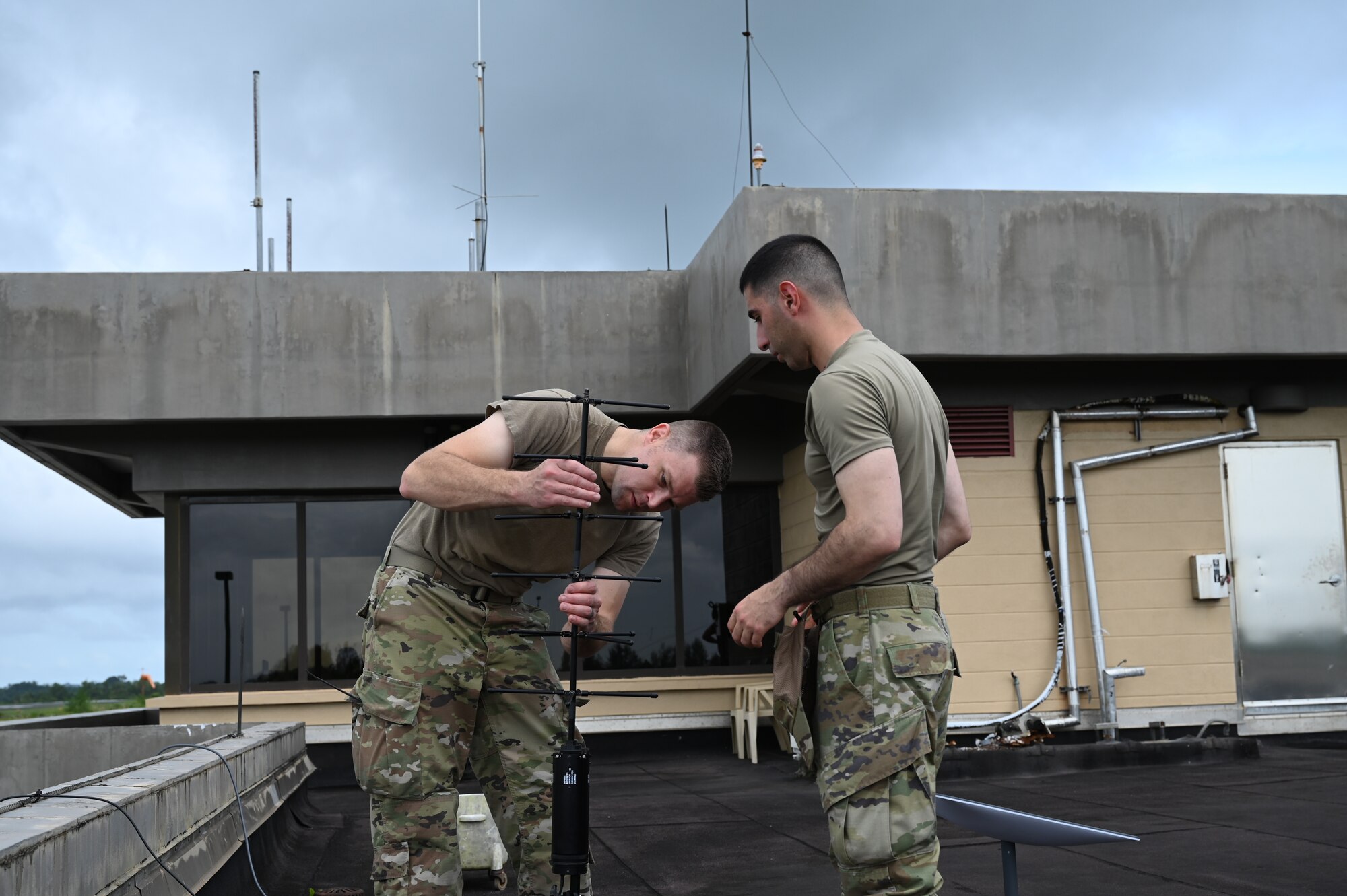two men wearing military uniforms set up a communications antenna outside
