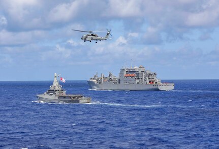 Two ships and a helicopter maneuver close to one another.