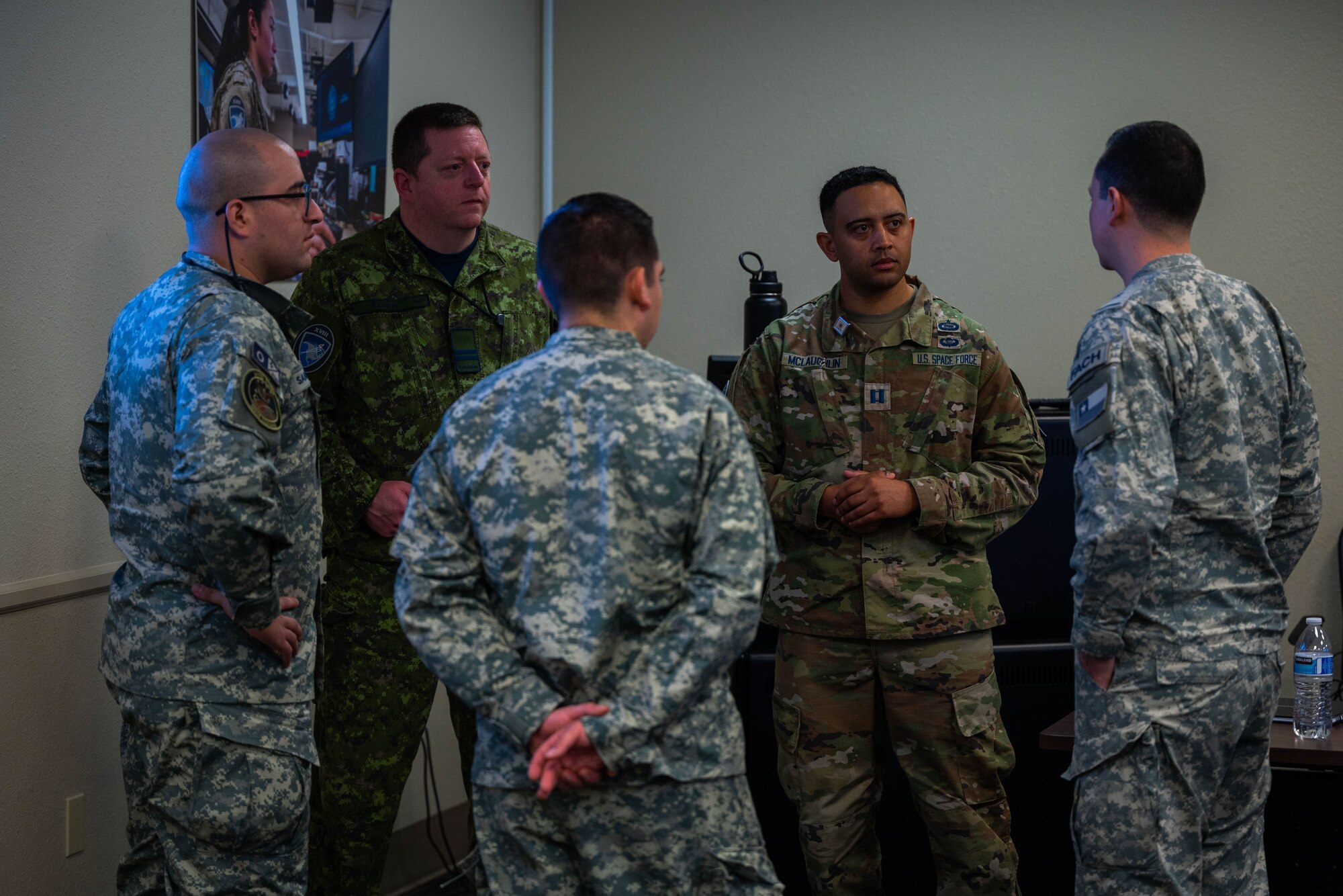 Five military members are standing in a room talking.