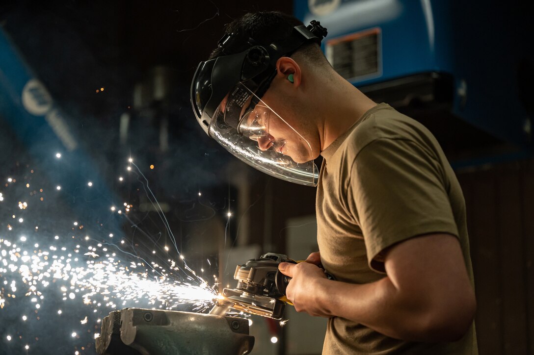 An airman uses an angle grinder causing sparks to fly.