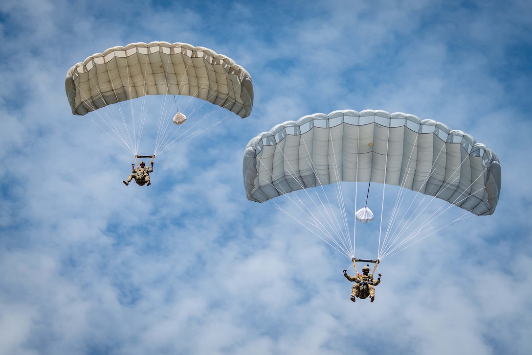 Two sailors using parachutes descend against a cloudy blue sky.